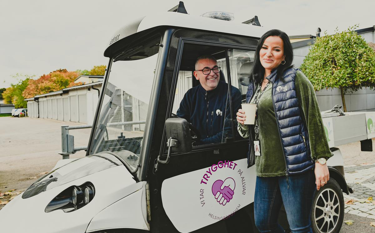 En man i en liten bil med texten "Vi tar trygghet på allvar" och en kvinna med en kaffemugg i handen. Båda jobbar för Helsingborgshem.
