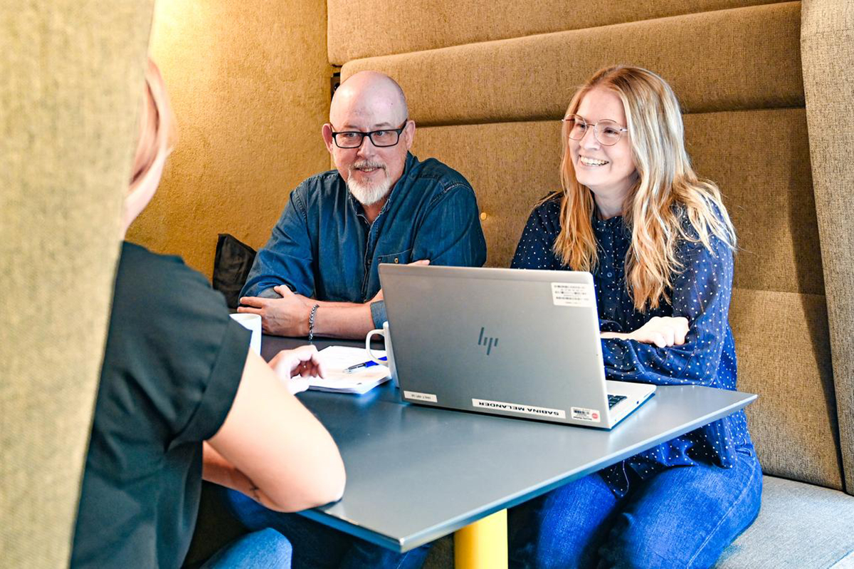 Tre av Helsingborgshems medarbetare sitter vid ett bord med en laptop