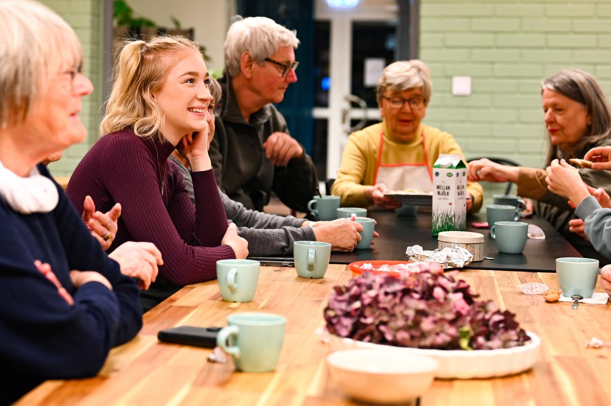 En grupp personer, både yngre och äldre fikar runt ett bord